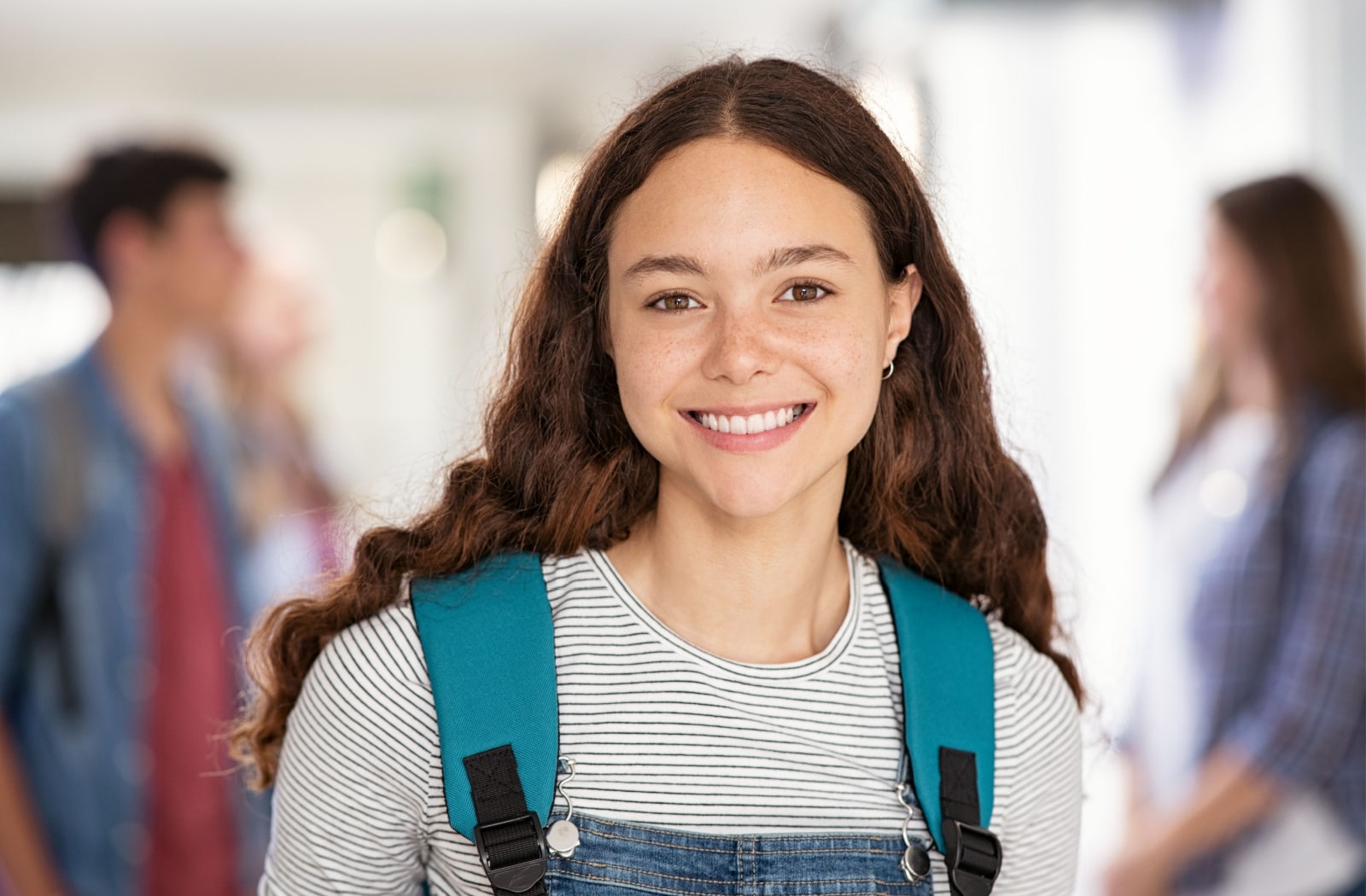 A teenage girl wearing a backpack smiles at the camera