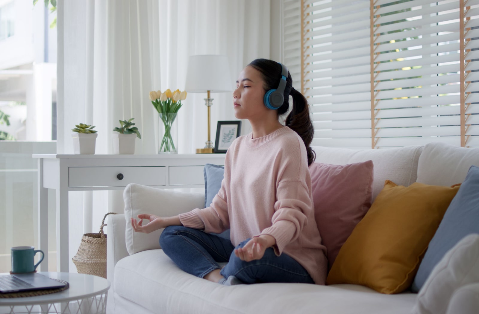 A teenage girl meditating on her couch and she is wearing headphones over her ears