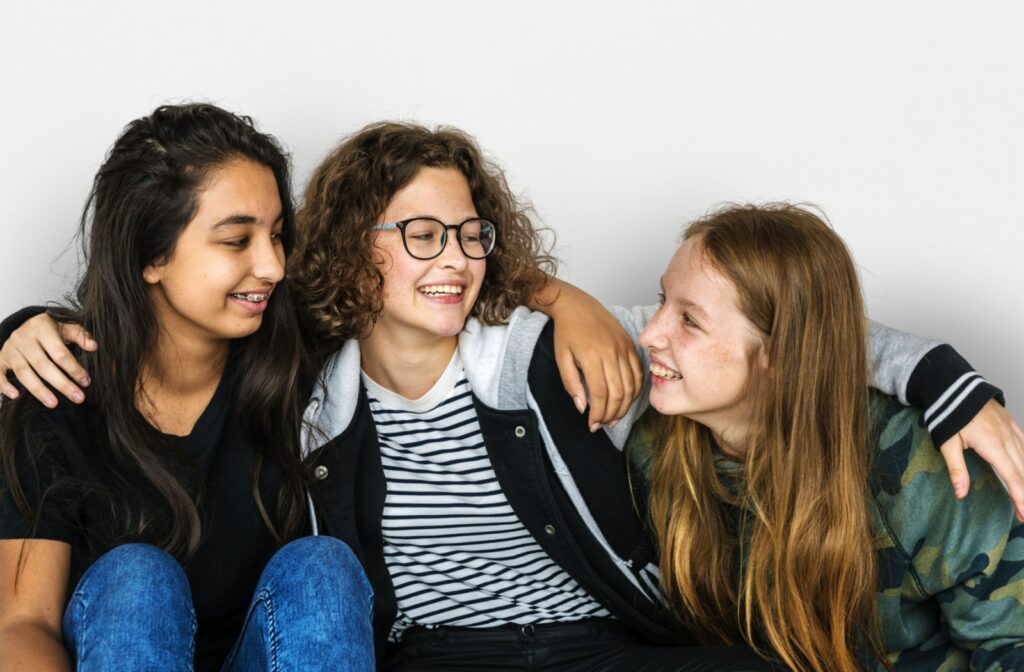 A group of three female teenage friends sitting together with their arms around each other