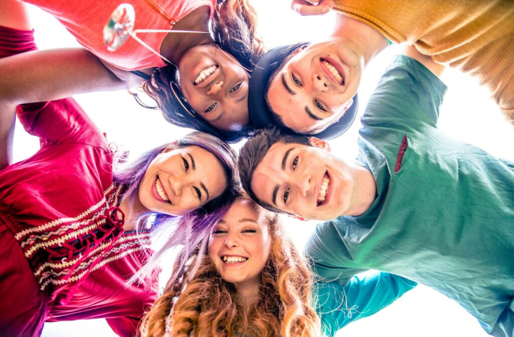 A group of five teenage friends standing together in a circle and smiling at the camera